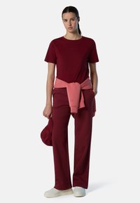 Camiseta burdeos y pantalones de pierna ancha a juego, acentuados con un suéter rosa atado a la cintura. Zapatillas blancas completan el conjunto.