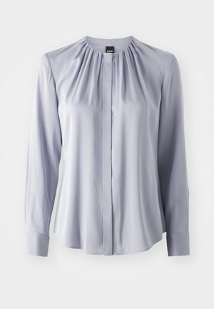 Lys grå langermet bluse med rynket halslinning, knappedetaljer foran og mansjetter. Laget av glatt stoff med en myk tekstur.