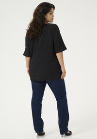 Tunique blouse noire texturée à manches trois-quarts, assortie à un jean droit bleu foncé et des chaussures à talons noires.