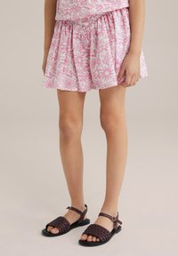 Rozā ziedu raksta svārki ar savelkamu jostasvietu, vilkti kopā ar tumši purpura ieaustām sandalēm ar potītes siksniņu un platu zoli.