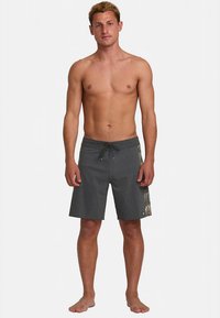 Sivé boardshorty s tkanou textúrou, s čiernou šnúrkou na stiahnutie a vzorom listov palmy na ľavej strane. Žiadne viditeľné vrecká.