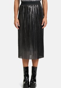 Schwarzer plissierter Midirock mit glänzender, metallischer Oberfläche; verfügt über einen breiten elastischen Bund und eine strukturierte Oberfläche. Getragen mit schwarzen Lackstiefeln.