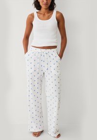 Witte pyjamabroek met blauwe hartpatronen, met een losse pasvorm, elastische tailleband en zijzakken; gecombineerd met een witte tanktop.