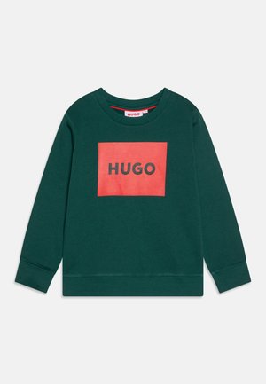 Sweatshirt vert avec un graphique rectangulaire rouge présentant le mot "HUGO" en noir. Design classique à col rond avec des poignets et un ourlet côtelés.