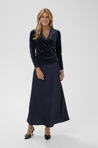 Top avvolgente in velluto blu navy a maniche lunghe abbinato a una gonna fluente blu navy. Tacchi alti neri con decorazioni completano l'outfit.