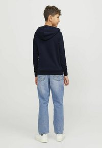 Sudadera navy con capucha, puños y dobladillo acanalados, combinada con jeans de pierna recta azul claro y zapatillas blancas, vista desde la parte de atrás.