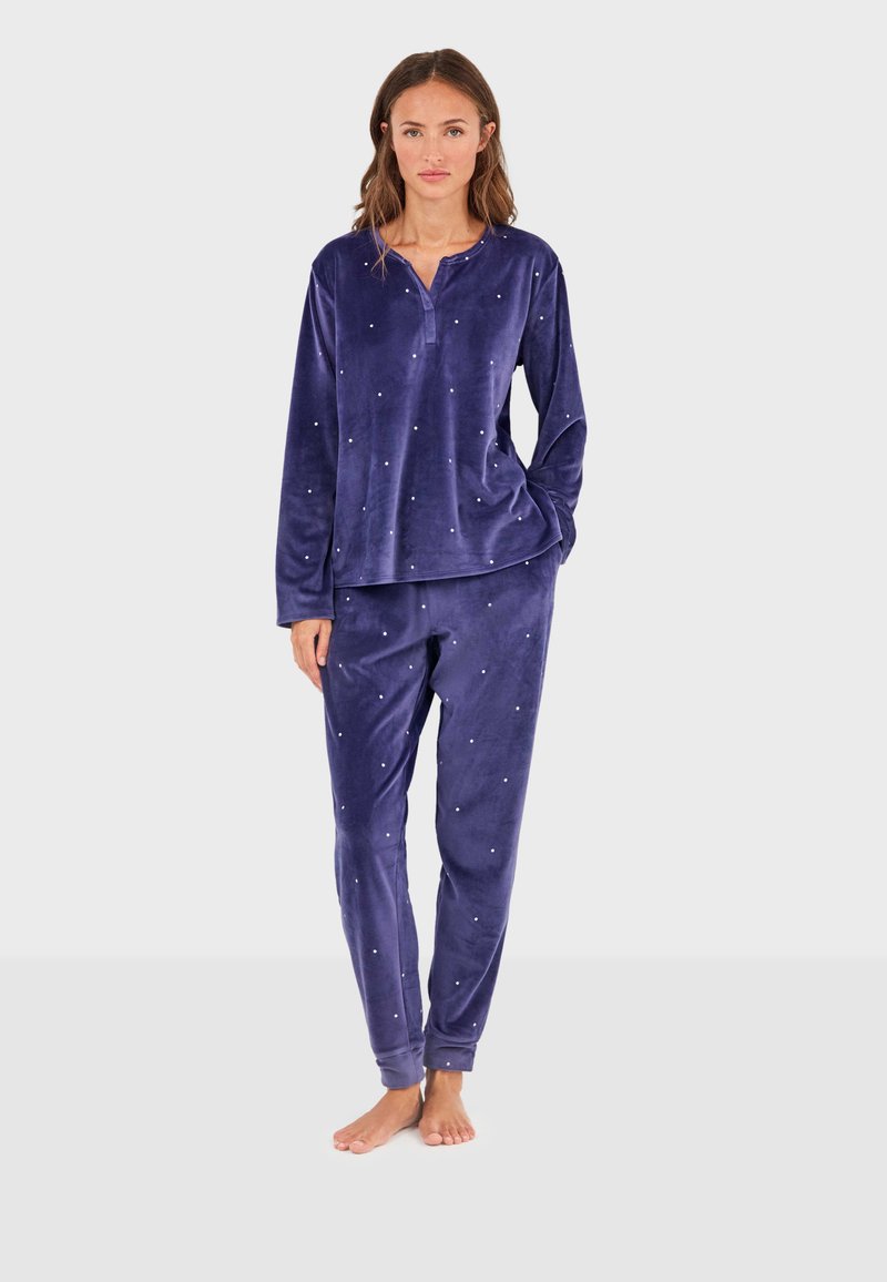 Pyjamas en velours violet comprenant un haut à manches longues avec un col henley et un pantalon orné de petits accents décoratifs. Coupe douce et décontractée.