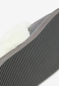 Pantoufle grise avec un doux revêtement en fourrure blanche, dessus en suède gris texturé et semelle en caoutchouc gris foncé striée pour une meilleure traction.