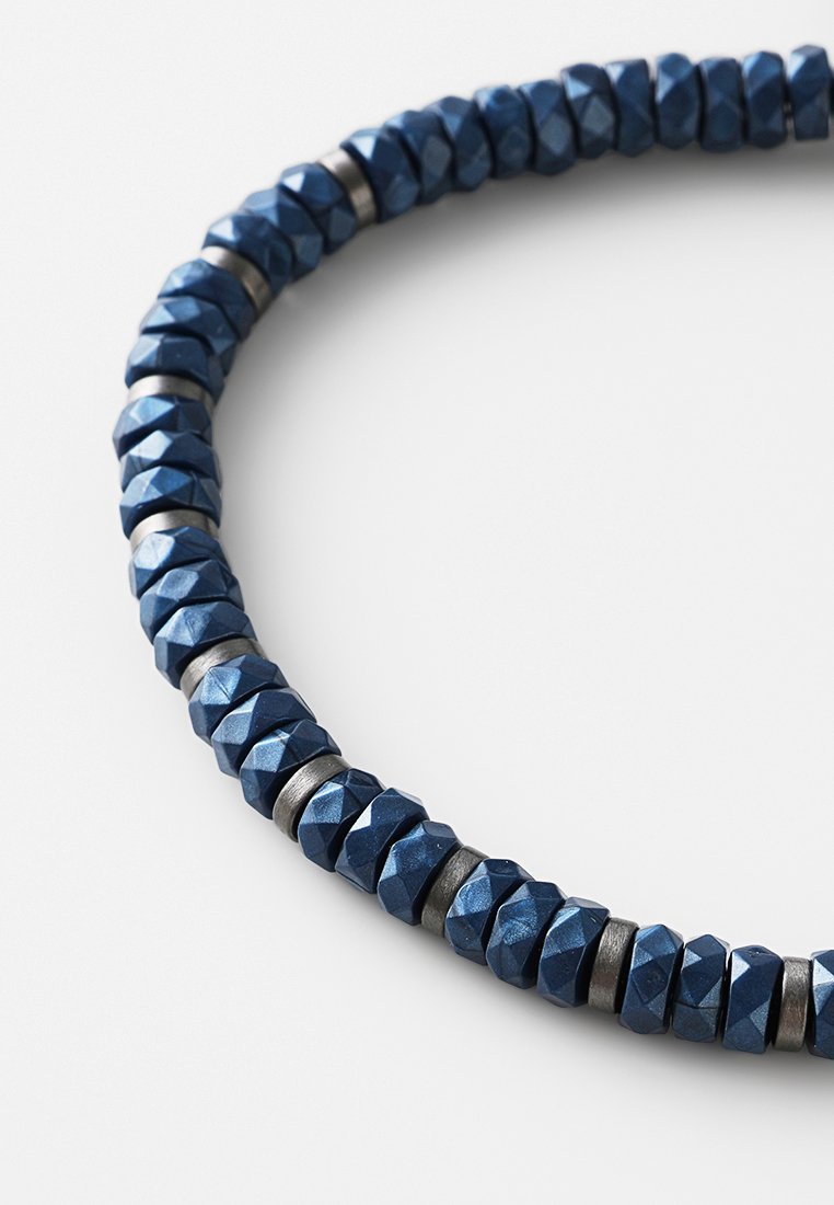 Eine marineblaue Perlenkette mit facettierten Perlen und metallischen Akzenten, die ein strukturiertes und geometrisches Muster erzeugen.