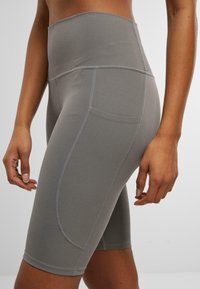 Graue hoch-taillierte Sportshorts aus dehnbarem Stoff, mit Flatlock-Nähten, seitlicher Tasche und einer glatten Textur.
