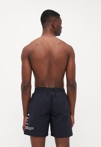 Costumi da bagno neri realizzati in materiale leggero, con una vita elastica, tasche laterali e testo stampato bianco sul lato sinistro.