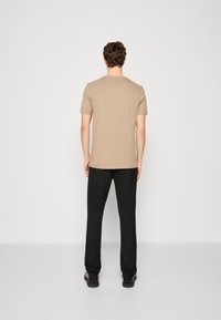 Beige t-shirt med korta ärmar, bomullsmaterial, avslappnad passform, enfärgad design, kombinerad med svarta byxor och svart skor, sedd bakifrån.