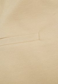 Tessuto beige con una piccola tasca orizzontale a welt caratterizzata da un'intrecciatura fitta e texture ravvicinata.