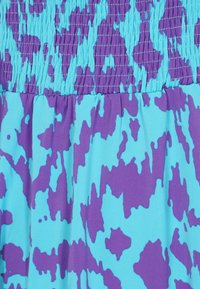 Färggklädsel med en strukturerad mönstring i lila och turkosa nyanser, med rynkade detaljer vid midjan och en slät tygfinish.