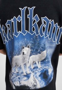 Svart t-skjorte med et blått og hvitt graphic av to ulver mot et snødekt landskap, med fet "karlkani" tekst over.