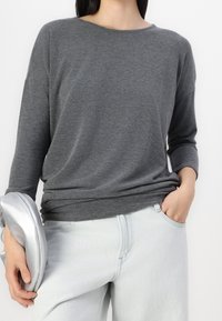 Maglia grigia chiara a maniche lunghe con scollatura ampia e vestibilità comoda, abbinata a pantaloni in denim azzurro chiaro. Design minimalista, texture morbida.