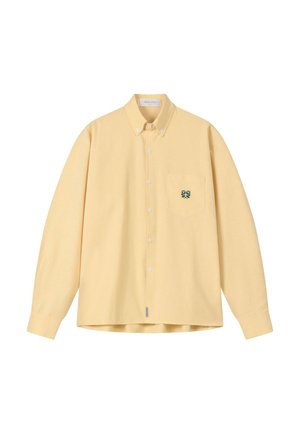 Bledozltá dlhá košeľa s gombíkmi, s golierom na gombíky a zelenou kvetinovou výšivkou na náprsnom vrecku.