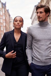 Svart pinstriped kostym med jacka och väst som bärs av en person, och grå turtleneck-tröja som bärs av en annan. Båda har moderna, välsittande designer.