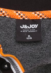 Grijze stofkraag met een oranje gevlochten rand. Zwarte label met witte tekst, een maatnummer en de merknaam "J&JOY." Patroon in de strepen van de kraag.