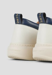 Sneaker in pelle bianche e navy con suola testurizzata. Presenta un tab sul tallone navy con il logo "ACBC" e un corpo bianco liscio con branding in rilievo.