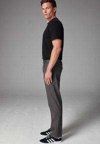 Sort t-shirt med korte ærmer, grå bukser og sorte sneakers med hvide striber. Bukserne har en glat tekstur og lige snit.