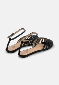 Schwarze Riemchensandalen mit einem geschwungenen Design, gefertigt aus strukturiertem Material. Verfügen über eine flache Sohle und einen Knöchelriemen mit einer Schnalle.