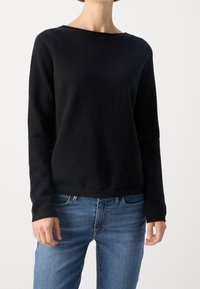 Czarny sweter z długim rękawem i szerokim dekoltem, wykonany z miękkiego materiału; zestawiony z niebieskimi dżinsami. Prosty fason o luźnym kroju.