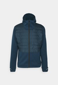 Veste hybride bleu marine avec un panneau supérieur matelassé, fermeture éclair intégrale et capuche. Fabriquée en tissu doux et texturé avec des poignets élastiques.