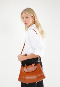 Braune Ledertasche mit runder Form, seitlichen Falten und einem oberen Deckel. Verfügt über einen langen Schultergurt und goldfarbene Hardware-Elemente.
