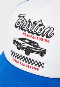 Adjustable baseball cap with a white front, blue brim. Features embroidered "Brixton Manufacturing," a black car graphic, and "Speed and Service."