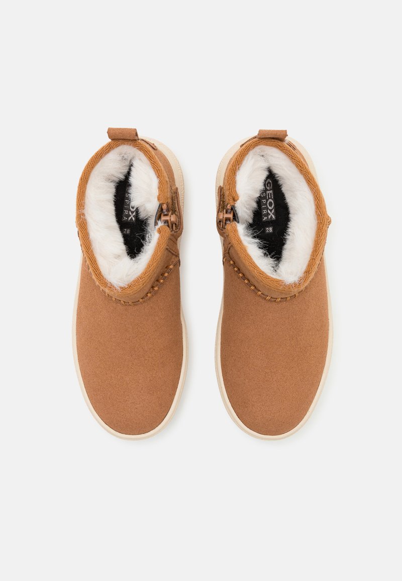 Botines marrones de tobillo hechos de tejido texturizado con forro de piel sintética. Cuentan con una cremallera en el lateral y una suela de goma beige.