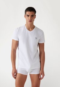 T-shirt bianco a maniche corte con scollatura a V, realizzato in tessuto morbido. Presenta un piccolo logo triangolare nero sulla parte sinistra del petto.