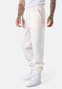 Weißer Jogginghose mit lockerer Passform, elastischem Bund und Kordelzug. Kombiniert mit weißen Sneakers, die eine glatte Stoffstruktur zeigen.