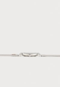 Stålur med slankt design, mesh-armbånd, rund skive og minimalistisk stil; har en enkelt krone på siden.