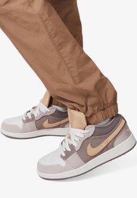 Idrettssko med en miks av grå, beige og hvite materialer. Har en teksturert overdel, polstret krage og en distinkt beige swoosh.