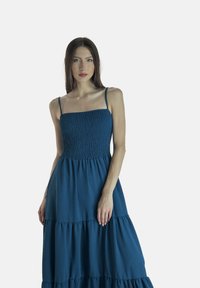 Abito maxi blu con corpetto a arricciato, spalline sottili e orlo a volant a strati. Realizzato in tessuto leggero, con una texture morbida.
