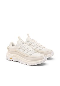 Beige sportskor med texturerad tygöverdel, elastiska snören och robust vit gummisula med tydligt mönster på sulan.