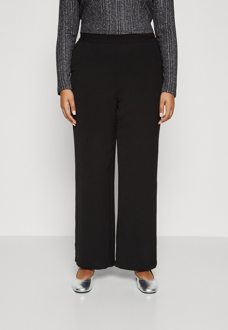 Pantalons larges noirs avec une finition texturée et une taille élastique, associés à un haut ajusté métallisé à manches longues et des ballerines argentées.