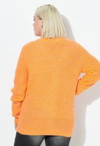 Maglione lavorato a maglia di un brillante arancione, con una vestibilità ampia, maniche lunghe, costine testurizzate e un collo arrotondato, completato da un orlo posteriore leggermente più lungo.