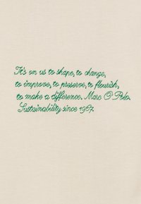 Tissu crème présentant un texte brodé vert avec un message de durabilité de Marc O'Polo, utilisant une police cursive.