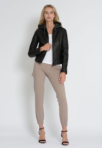 Zwarte leren jas met grijze capuchon, rits aan de voorkant, aansluitend ontwerp. Gecombineerd met beige joggingsbroek met zijzakken en zwarte hoge hakken.