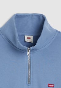 Ljust blå kvartdragning med ribbad krage, slät yta och liten röd Levi's-logga på vänster bröst. Silverfärgad dragkedja.