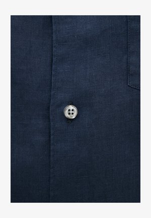 Tissu de chemise en lin marine avec un seul bouton en argent comportant quatre trous, positionné sur la patte de boutonnage avec un tissage texturé.