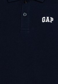 Námornícky pólový tričko vyrobené z bavlneného zmesi, s trojbuttonovým zapínaním a bielym vyšívaným logom "GAP" na ľavej strane hrude.