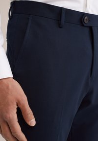 Pantalons navy avec une texture de tissu lisse. Design ajusté avec un devant plat, des poches latérales et une fermeture à bouton à la taille.