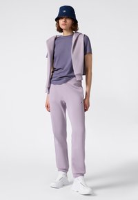 Conjunto deportivo lila que incluye una camiseta de manga corta, joggers a juego con puños acanalados y un sombrero nautico azul marino. Zapatillas blancas completan el look.
