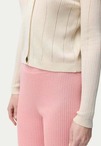 Ribbad stickad kofta i krämfärg med knappstängning, i kombination med ribbade rosa leggings. Har mjuk textur och figurnära siluett.