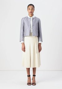 Lilla mønstret cropped jakke med knappelukking, parret med en hvit skjorte med krage og en kremfarget lang skjørt, ferdig med svarte ankelrem-sko.