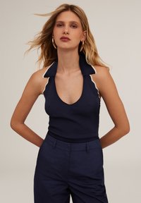 Marinblå ribbad linne med djup V-ringning och kontrasterande krämfärgad kant vid kragen. Matchas med marinblå högmidjade byxor.