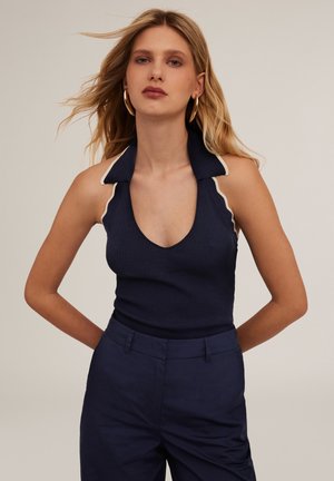 Top in cotone a coste blu navy con scollatura a V profonda e bordo in crema di contrasto sul colletto. Abbinato a pantaloni blu navy a vita alta.